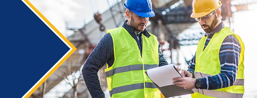 Two engineers wearing hard hats and safety vests consulting a clipboard