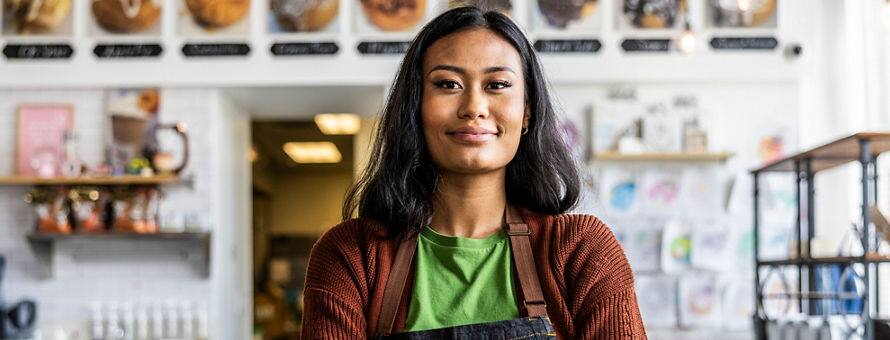 An entrepreneur wearing an apron standing in front of a desk in her business.