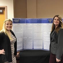 Two undergraduate students in front of a large poster displaying their research.