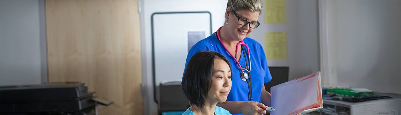 2017 online nursing degree graduate Kristina Libby looking over the shoulder of a fellow nurse in a medical office.