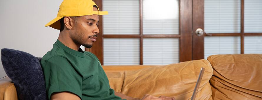 Keyon Tuiteleleapaga, an SNHU graduate with a bachelor's in human services and master's in psychology, using a laptop on his couch.