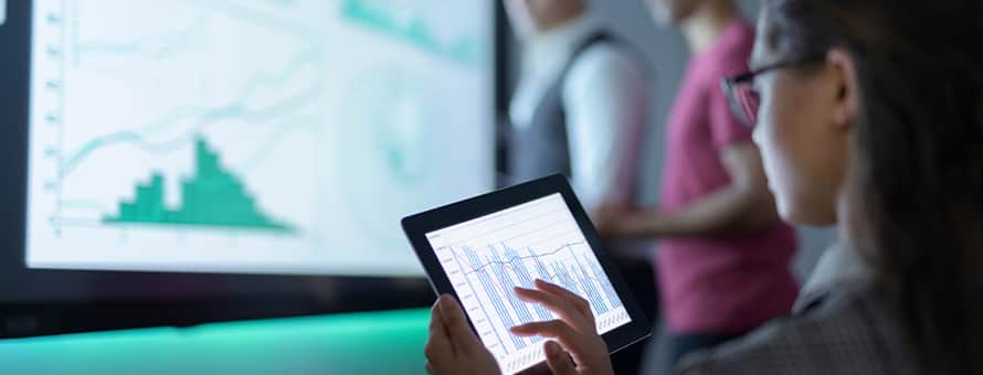 A woman with dark hair and glasses looking at data about what you can do with a finance degree on a tablet.