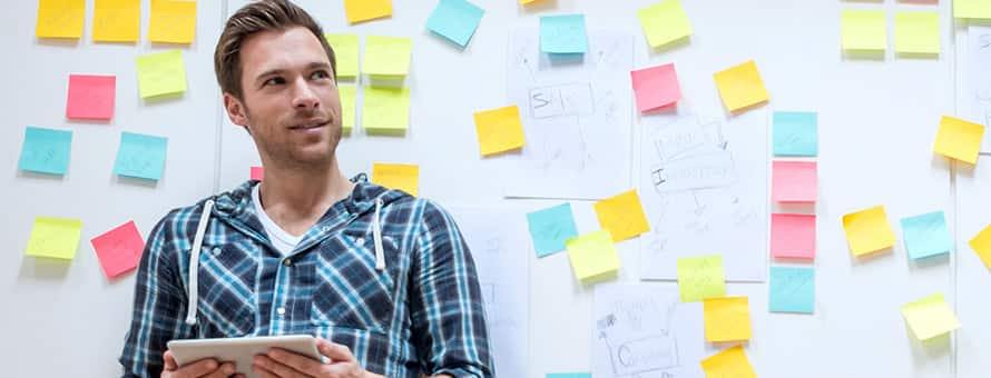 Man standing in front of a wall of sticky notes, holding a tablet researching what career to choose