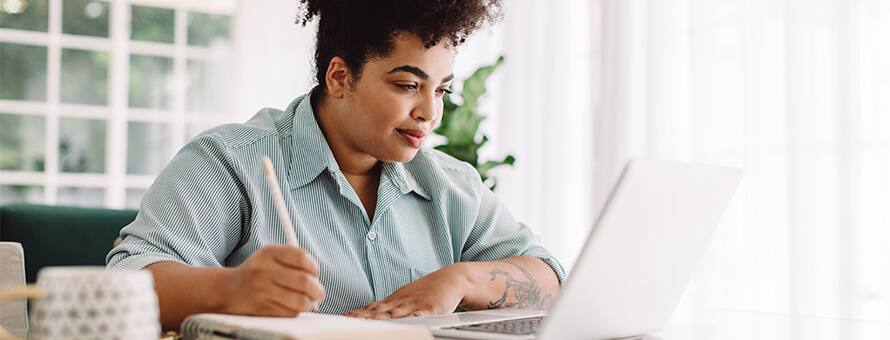 A student sitting at a desk taking notes off a laptop