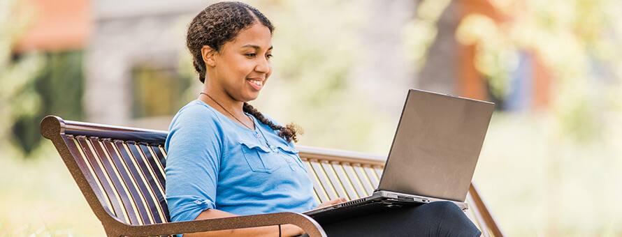 A person sitting on a bench, researching what an undergraduate degree is on a laptop.