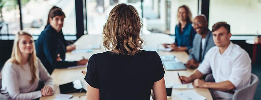 A manager standing at the head of a conference table presenting what an mba is to her team