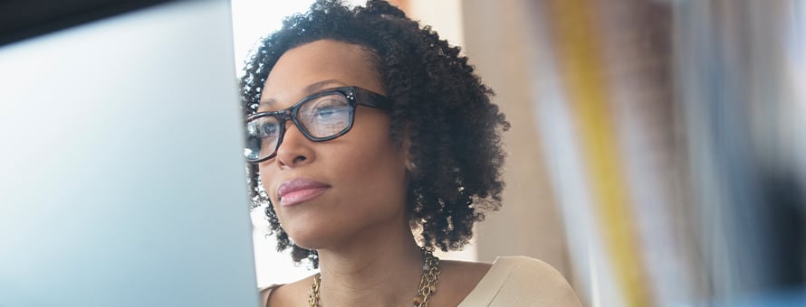 A woman with glasses on sitting at her laptop researching terminal degrees