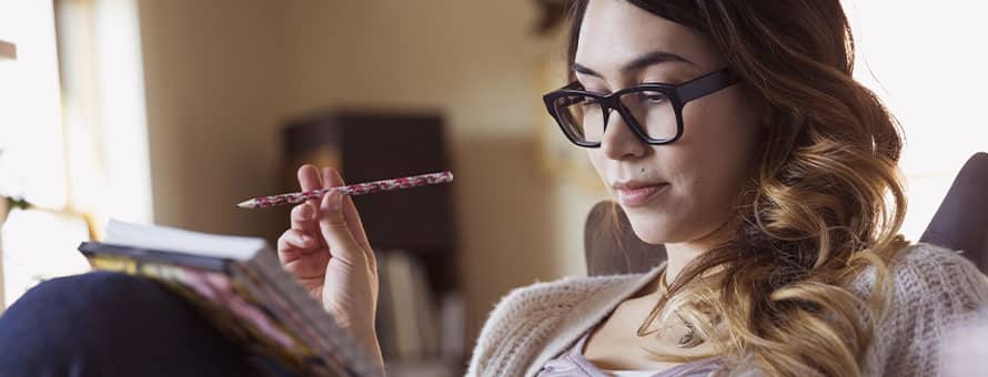 A woman wearing glasses reading a creative writing piece in a notebook.