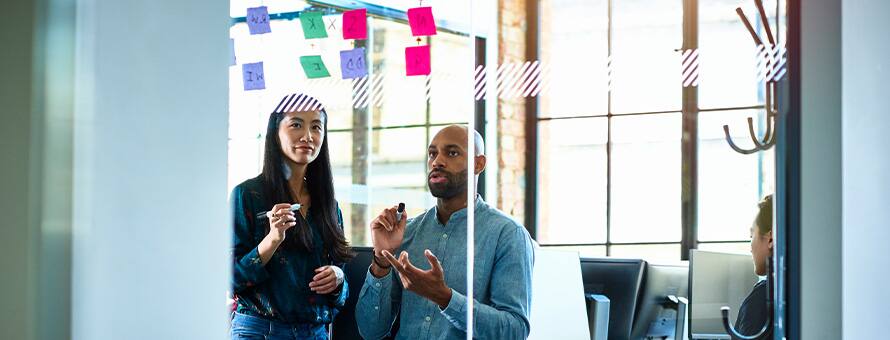 A man and a woman using a whiteboard and sticky notes to map a project.