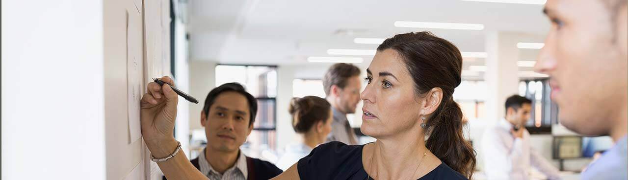 A business woman writing on a poster board while others look on