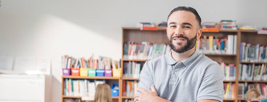 An image of a man smiling in front of bookshelves.