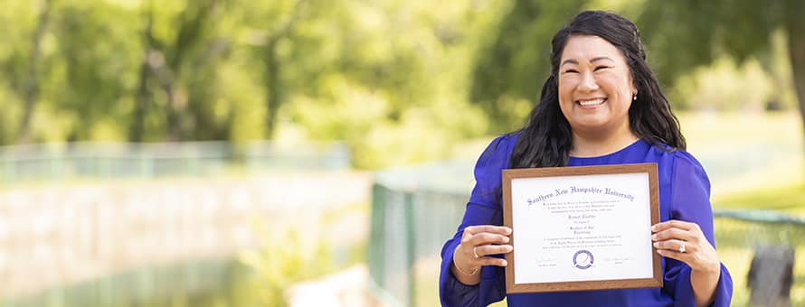 Jennet Trotter, who finished her degree at SNHU, holds her framed diploma while posing in a park.
