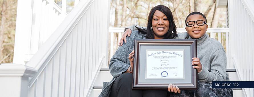 Human services graduate Mo Gray sitting on steps with her son. They are holding up her SNHU diploma and smiling