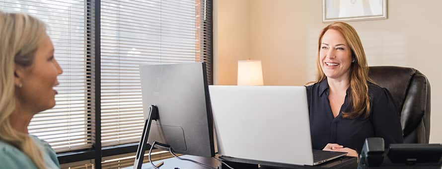 A healthcare professional behind a desk talking to a patient and smiling