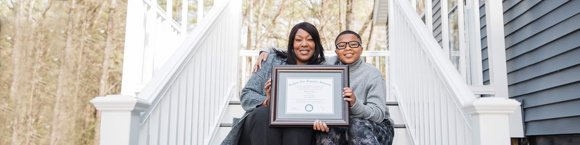 A SNHU graduate holding her diploma on a porch with her child