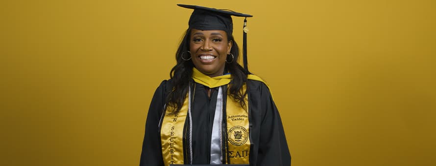 An SNHU graduate wearing an honor society stole and holding her diploma at her commencement ceremony.