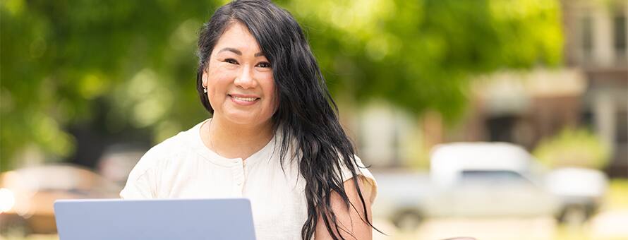 A student choosing a college on her laptop while outdoors.