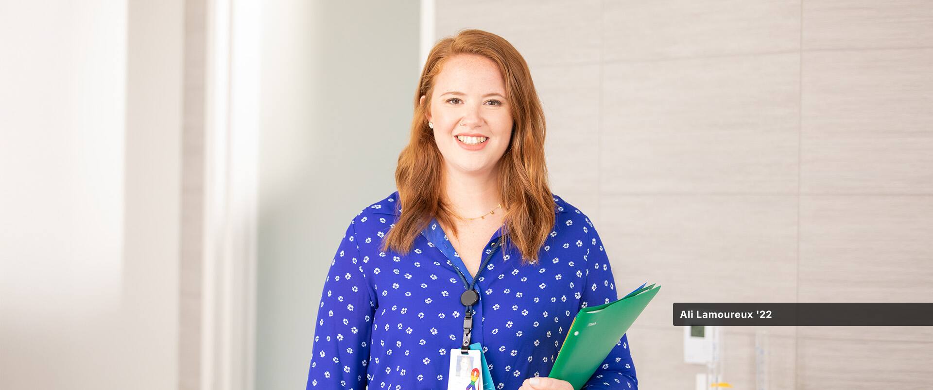 Ali Lamoureux-Rule, who earned her healthcare administration degree from SNHU in 2022, wearing a blue and white blouse and holding a green folder in her left arm.
