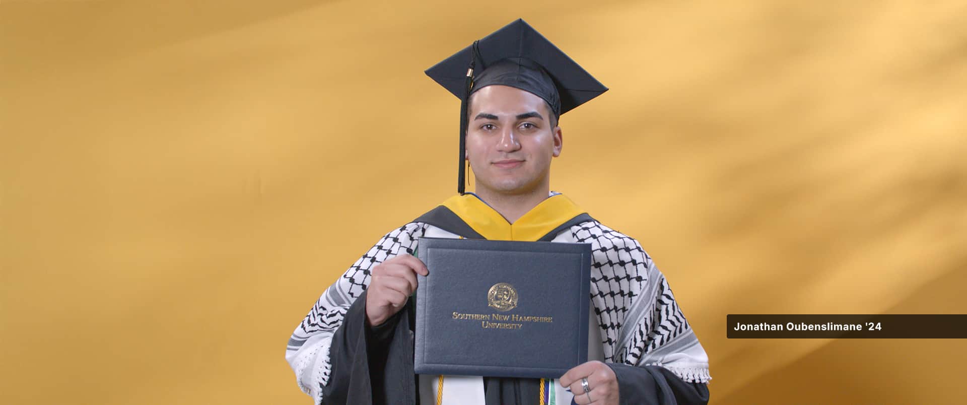 Jonathan Oubenslimane, who earned his bachelor's in business administration with a concentration in entrepreneurship in 2024, wearing his cap and gown and holding his diploma.