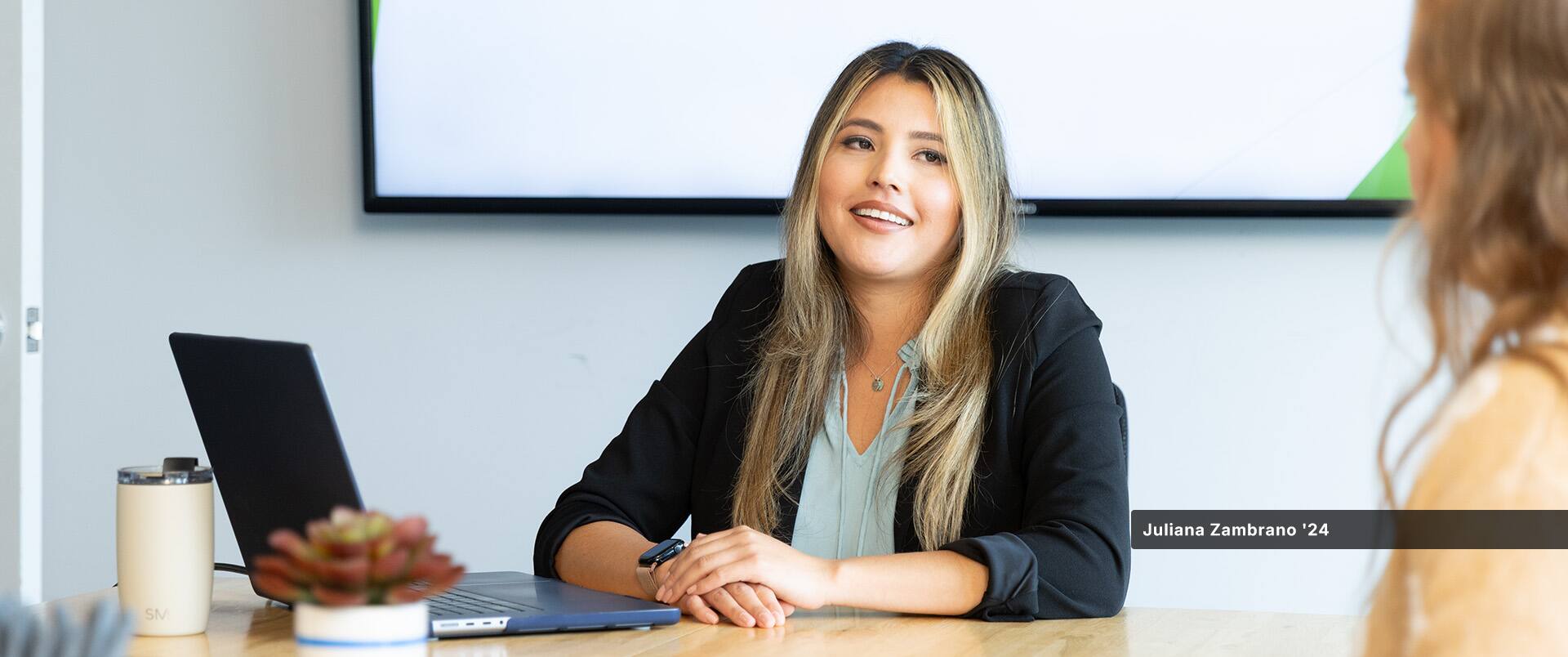 Juliana Zambrano, who earned her bachelor's in business administration with a concentration in project management from SNHU in 2024, speaking to another woman at a table with a laptop open in front of her.