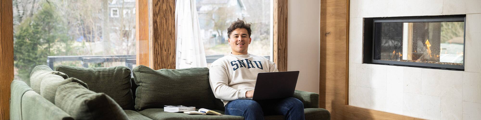SNHU student Kevin Bucardo '25MBA sitting on a green couch using a laptop.