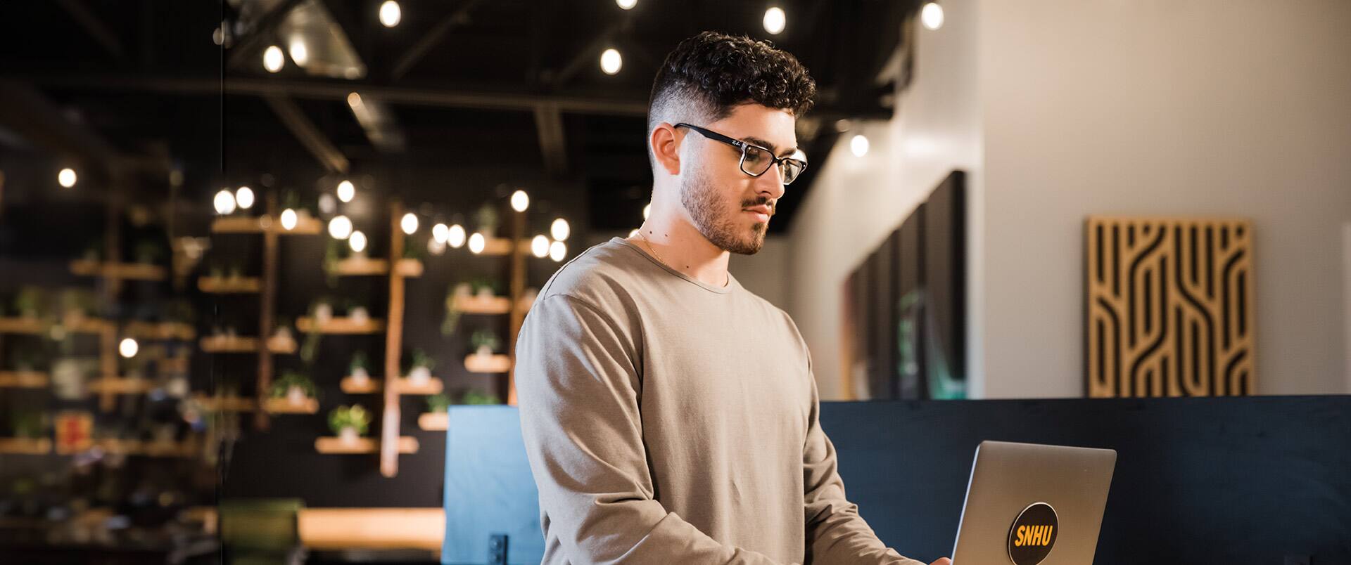 Naeem Jaraysi, who earned a marketing degree in 2021, standing and working on a laptop with an SNHU sticker on the front.
