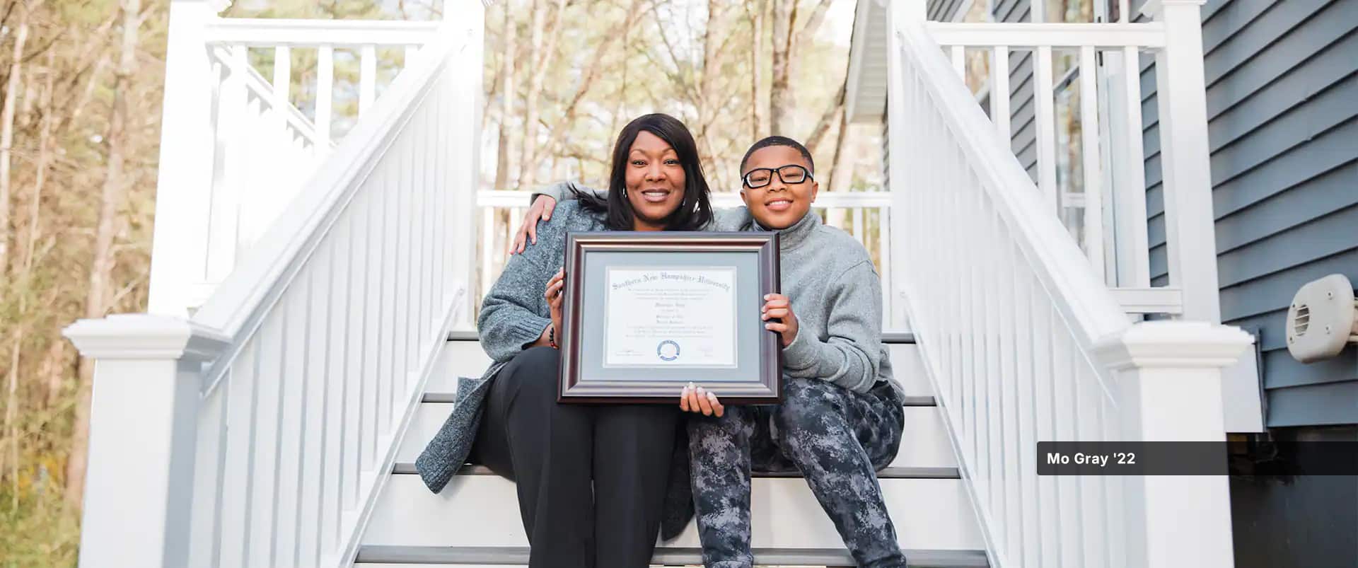 Mo Gray, holding her 2022 online human services degree diploma, while sitting next to her son on a staircase.