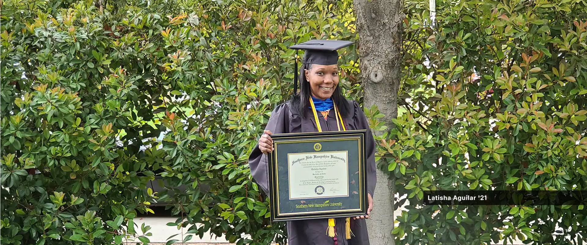 Latisha Aguilar, who earned her bachelor's in psychology with a concentration in child and adolescent development, wearing her cap and gown and holding her framed diploma.