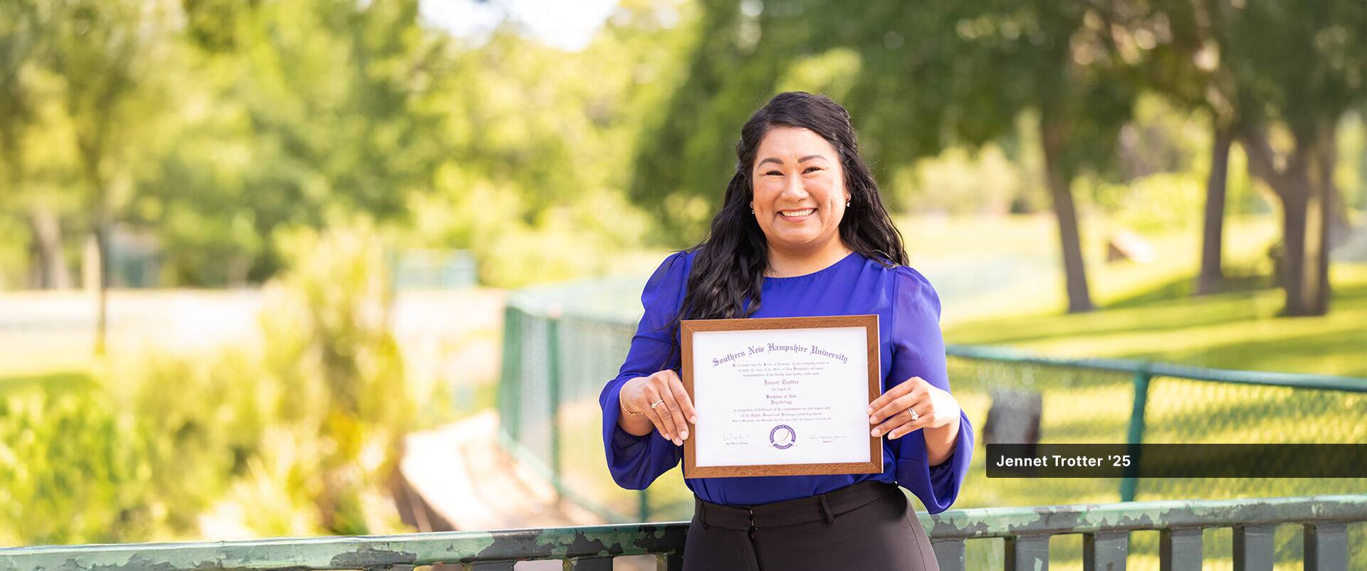 Jennet Trotter, who earned her online bachelor's in psychology in 2025, wearing a blue blouse and holding her framed diploma.