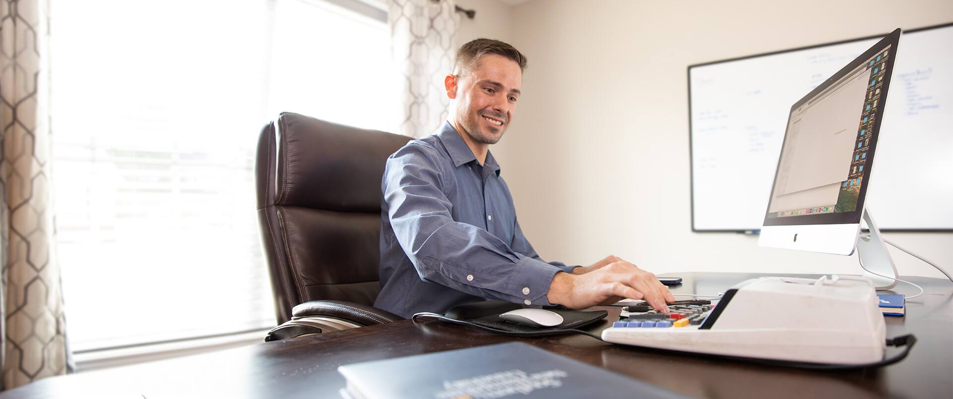 Blake Venable, who earned his bachelor's in accounting in 2023, with a computer keyboard and calculator on a desk in front of him and a whiteboard on the wall in the background.