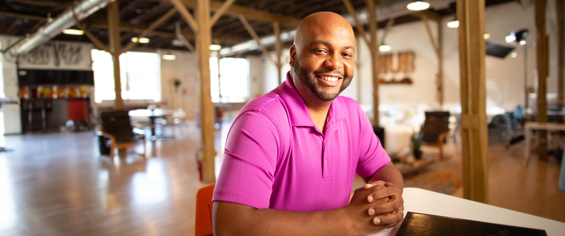 Montre Everett, wearing a pink polo shirt standing in a large open room with his hands clasped in front of him.