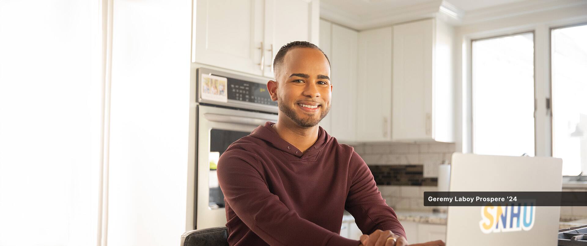 An online SNHU student sitting at a kitchen table with a laptop.