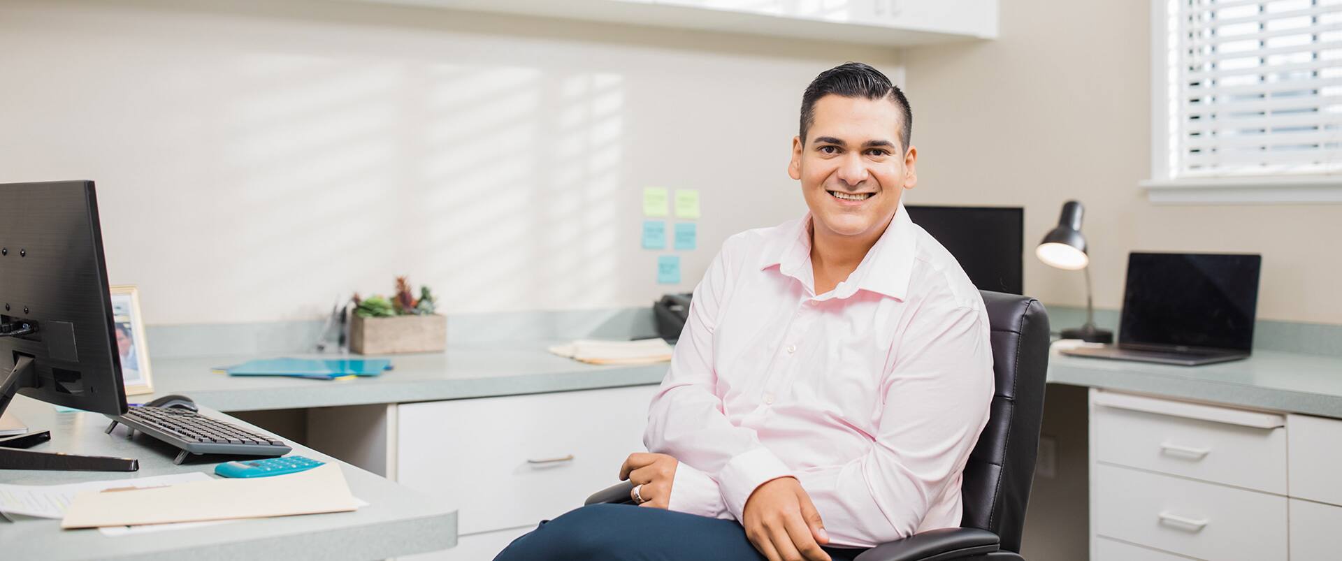 Juan Muños, who earned his degree from SNHU in 2022, sitting in an office chair with one leg crossed  over the other.