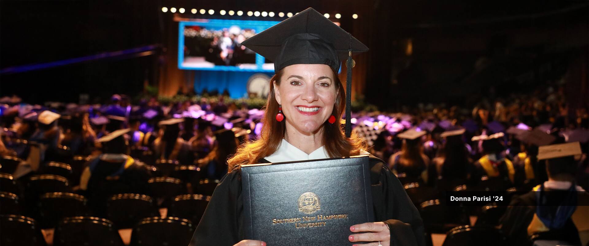 Donna Parisi, who earned her master's in English and creative writing in 2024, wearing her cap and gown and holding her diploma.