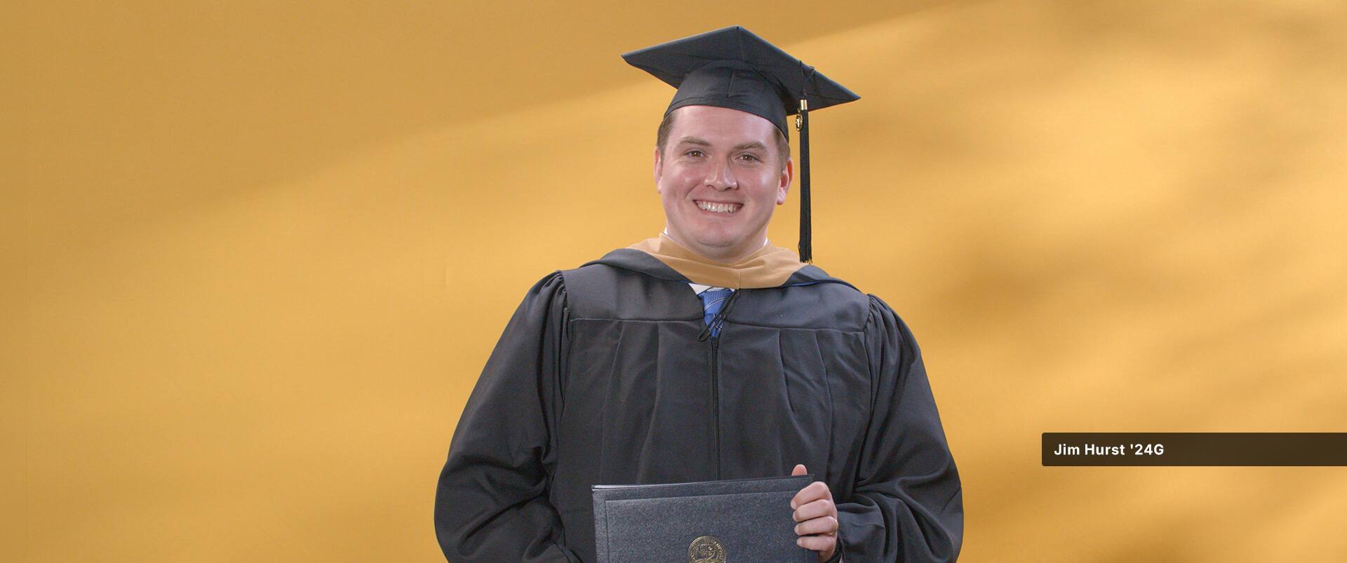 Jim Hurst, who earned his online MBA with a concentration in Finance from SNHU in 2024, wearing his cap and gown and holding his diploma.