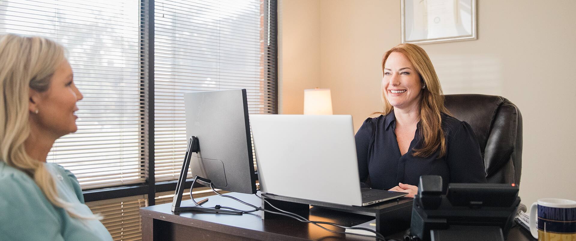 Nikki Bennett, who earned her degree at SNHU, sitting behind a desk with a laptop and computer monitor in front of her speaking to another woman.