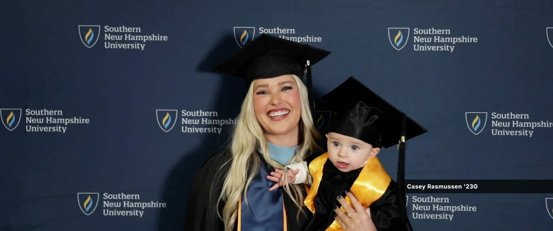 Casey Rasmussen, a 2023 graduate who earned her master's in education degree at SNHU, wearing her graduation robe and holding son.