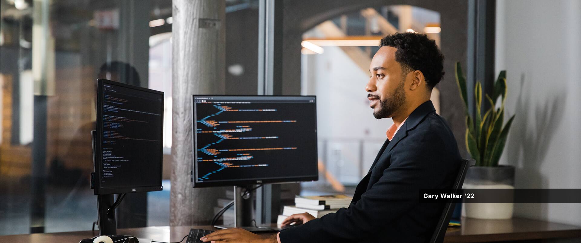 SNHU graduate Gary Walker '22 sitting at a desk with two computer monitors that are displaying computer code.
