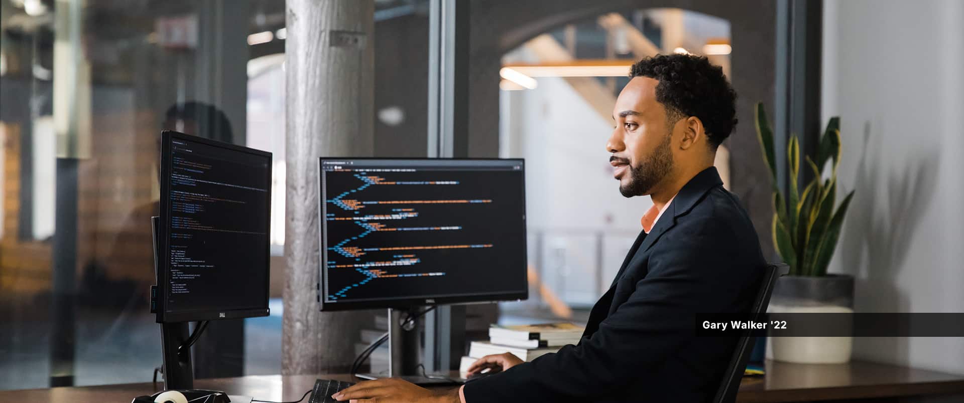 SNHU graduate Gary Walker '22 sitting at a desk with two computer monitors that are displaying computer code.