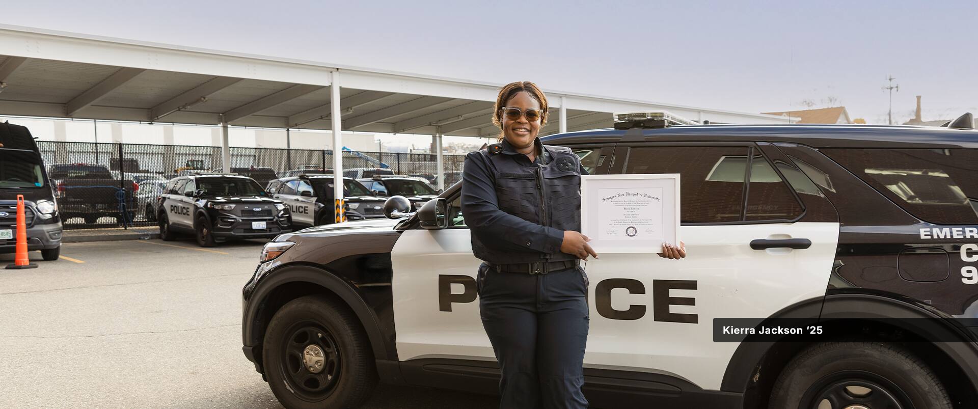 Kierra Jackson, who earned online criminal justice degrees from SNHU in 2024 and 2025, holding her framed diploma standing in front of a police cruiser.