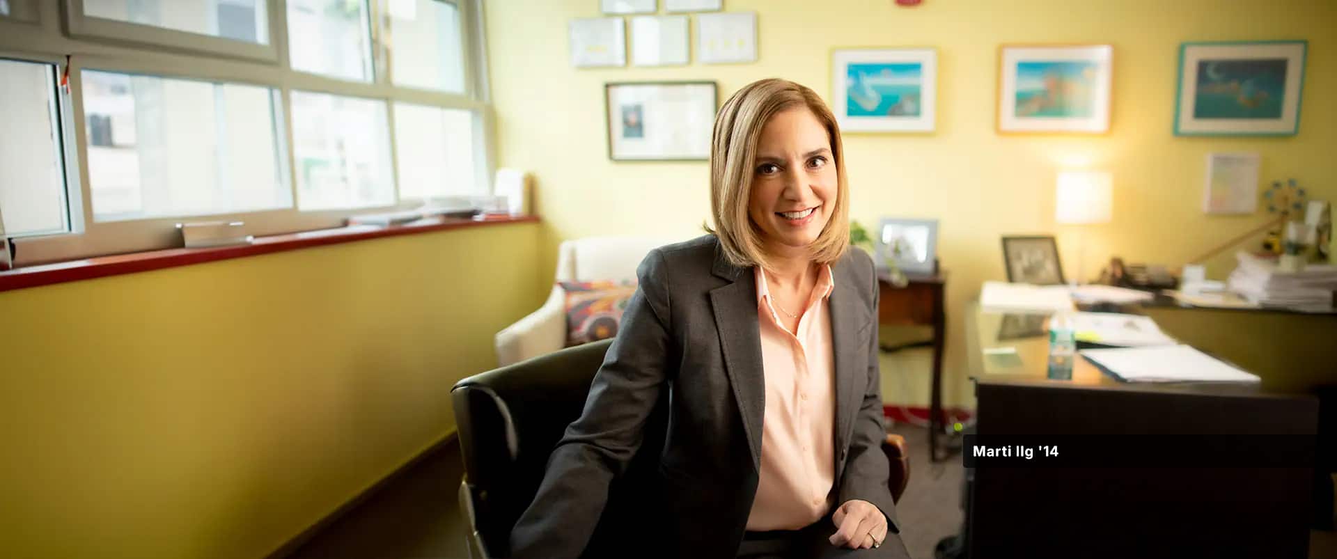 Marti Ilg, who earned her degree from SNHU in 2014, wearing a peach colored blouse and dark blazer sitting in a swivel chair next to a desk in her office.