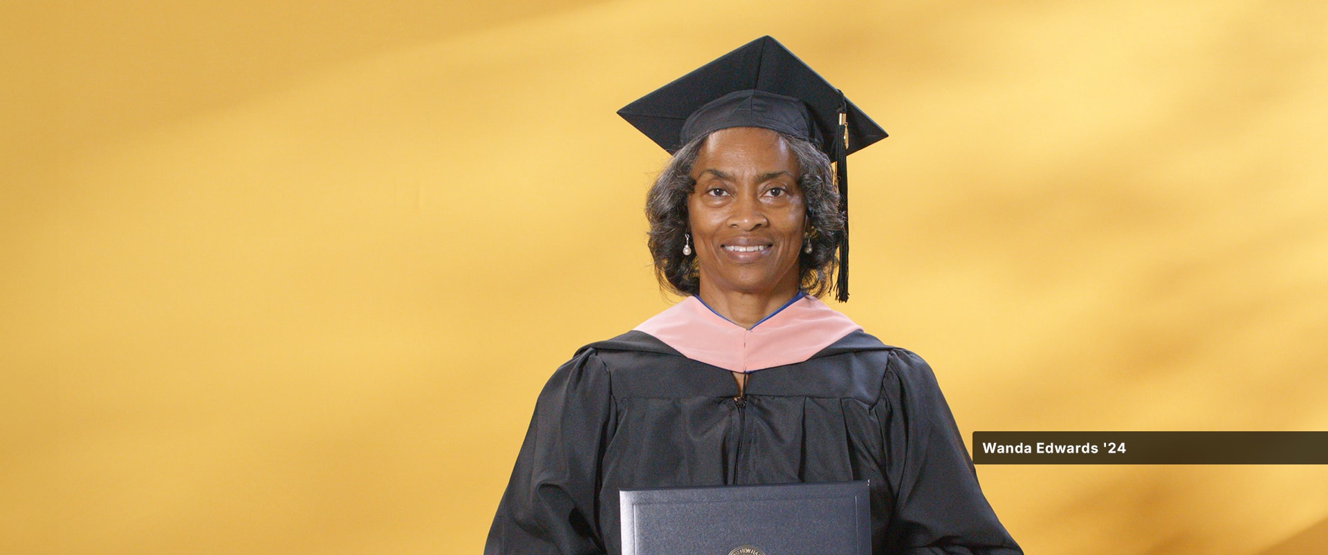 Wanda Edwards, who earned her Master of Public Health degree in 2024, wearing her cap and gown and holding her diploma.