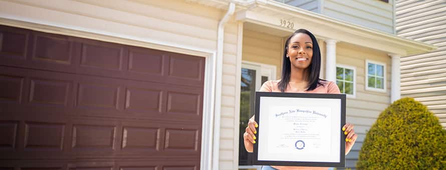 Minda Thurman, who has earned her Associate and Bachelor’s degrees at SNHU, standing in front of her home with her diploma. 