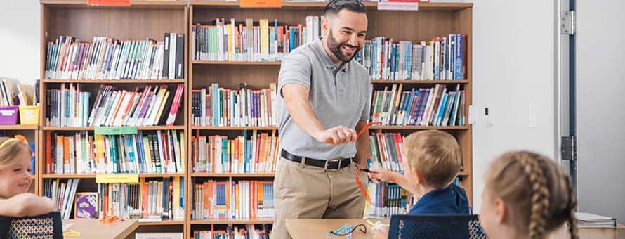A man and three children playing with pipe cleaners with crowded bookshelves in the background.