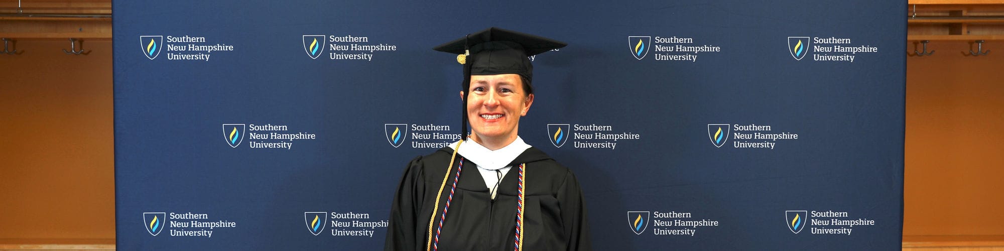Lisa Rogers, a Nebraska resident who earned her degree at SNHU, standing in front of step and repeat banner wearing her cap and gown.