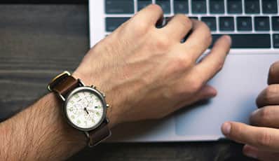A person's hands as they type on their laptop and check the time on their watch