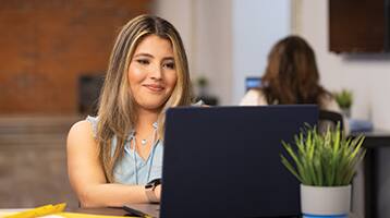 Juliana Zambrano, who earned her online bachelor's in business administration from SNHU in 2024, typing on her laptop with a small plant in front of her.