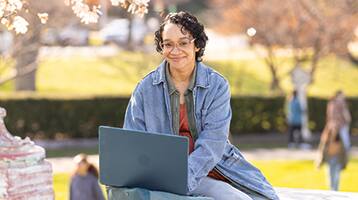 Michelle LitteJohn, who earned her online bachelor's in graphic design from SNHU in 2024, wearing a blue jacket while sitting outside typing on her laptop.