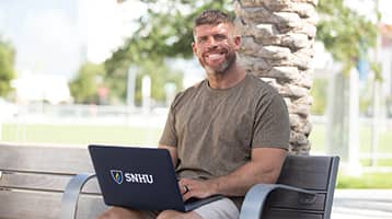 Stephen Kupryk, who earned his online bachelor's in psychology from SNHU, on a park bench with a laptop on his lap.