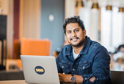 A man sitting at a desk with an SNHU laptop and smiling